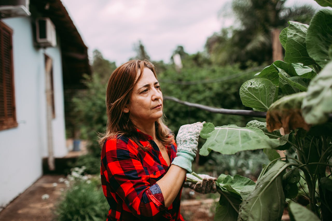 A woman tending her garden outdoors, wearing gloves and a plaid shirt.